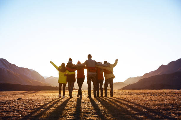 Group of happy friends stands and hugs against sunset mountains Group of happy friends stands and hugs against sunset mountains